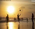 Plaża o zachodzie słońca, z ludźmi uprawiania sportu na brzegu, surferami i innymi na wodzie